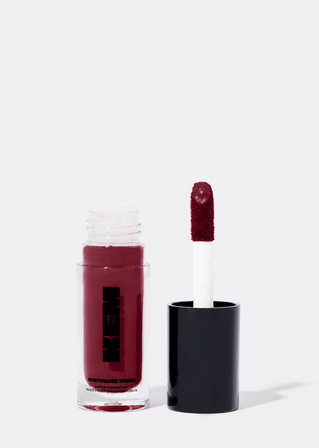 A bottle of KEM makeup liquid lipstick in a deep berry red shade, shown next to its applicator wand with a black cap on a clean white background.